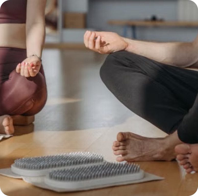 A wellness practitioner sitting cross-legged beside acupressure mats